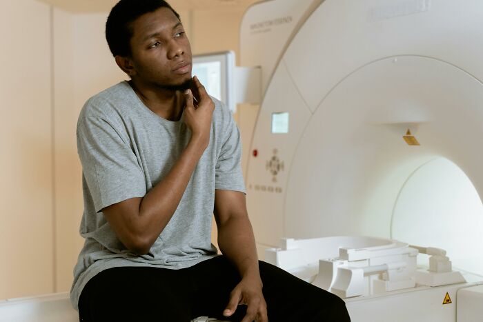 A man sitting pensively near an MRI machine, reflecting on life updates after marrying out of pressure.