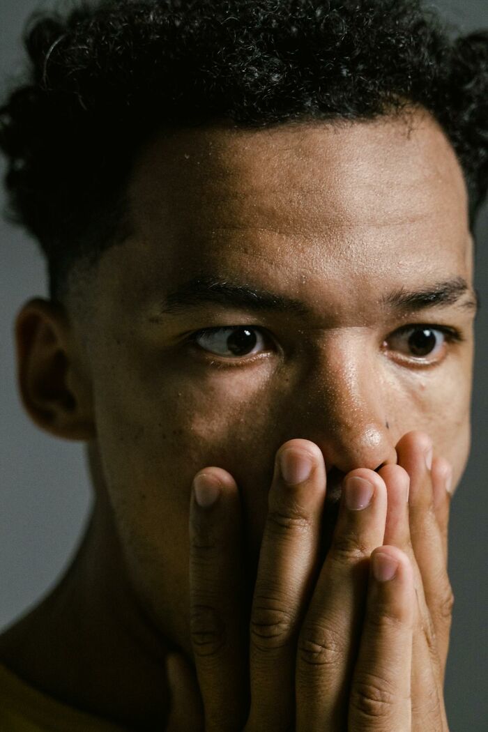 Young man with curly hair covering his mouth, showing fear while listening to creepy stories in the dark woods. Young man with curly hair covering his mouth, showing fear while listening to creepy stories in the dark woods.