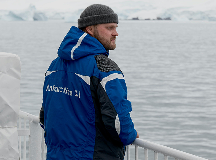 Man in blue Antarctica jacket and gray beanie looking out over cold ocean, symbolizing long-distance romance abroad. Man in blue Antarctica jacket and gray beanie looking out over cold ocean, symbolizing long-distance romance abroad.