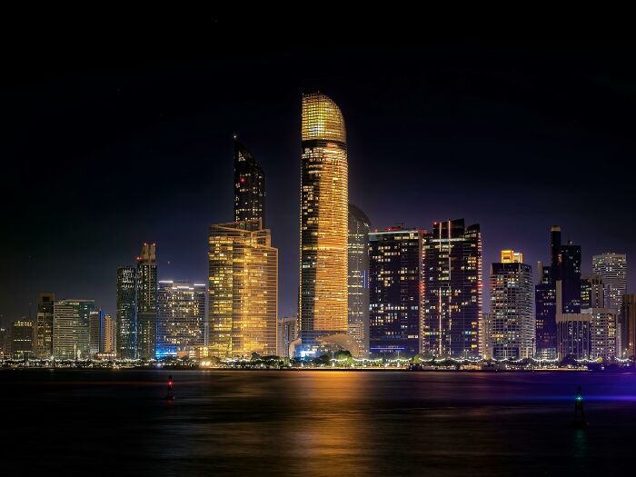 Night skyline of a city with illuminated skyscrapers reflecting on water, showcasing former capitals in a sneaky urban view. Night skyline of a city with illuminated skyscrapers reflecting on water, showcasing former capitals in a sneaky urban view.