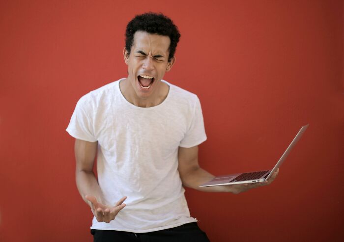 Young man frustrated holding laptop, reacting to tricky questions challenge against solid red background. Young man frustrated holding laptop, reacting to tricky questions challenge against solid red background.
