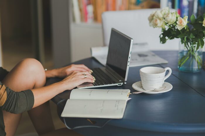Person typing on laptop with notebook and coffee cup on table, reflecting on time spent on pointless tasks