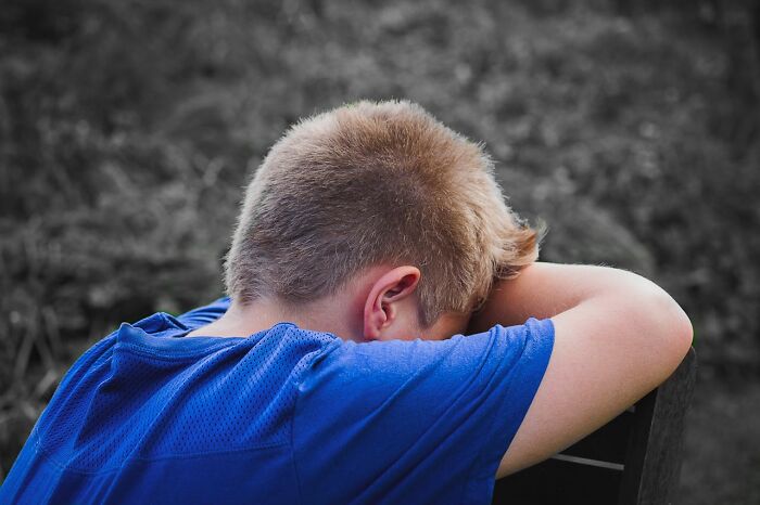 Young boy in blue shirt resting head on arms outside, illustrating gender differences in what women are allowed to do.