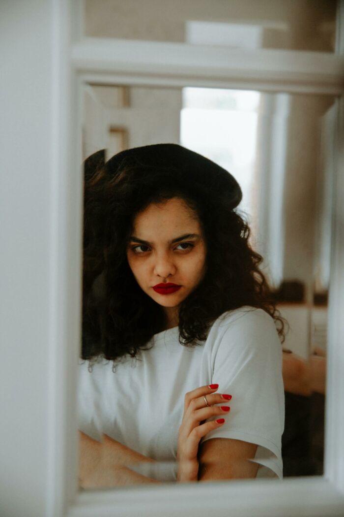 Young woman with curly hair and red lipstick looking serious through a window, highlighting women restrictions and gender inequality.