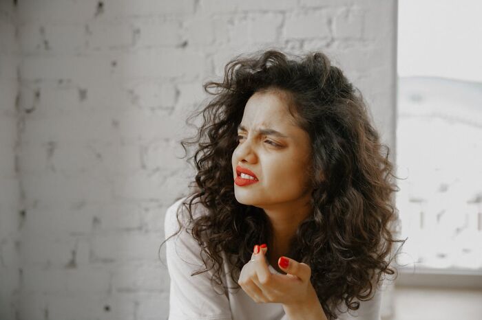 Woman with curly hair and red lipstick looking concerned, illustrating things women are not allowed to do freely.