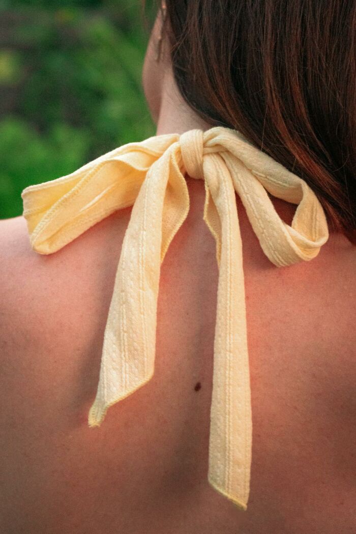 Close-up of a tied yellow fabric bow on a person's back with blurred green woods background. Close-up of a tied yellow fabric bow on a person's back with blurred green woods background.