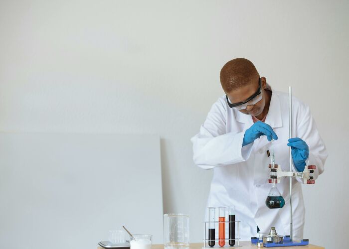 Scientist in a white lab coat and blue gloves conducting a chemistry experiment with test tubes and a flask. Scientist in a white lab coat and blue gloves conducting a chemistry experiment with test tubes and a flask.