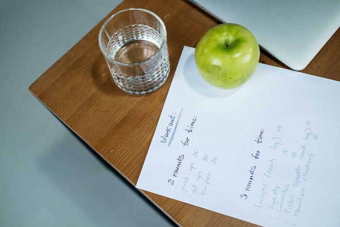 Glass of water, green apple, and handwritten workout plan on a desk symbolizing pointless time spent activities.