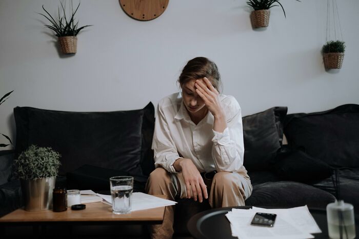 A stressed person sitting on a couch with head in hand, surrounded by papers and a glass of water, sharing secrets.