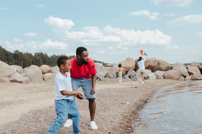A father and son skipping stones by the water, illustrating differences in things women are not allowed to do.