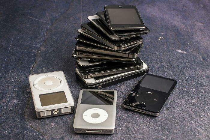 Stack of outdated smartphones and classic iPods on a textured surface, representing time spent on obsolete tech devices.