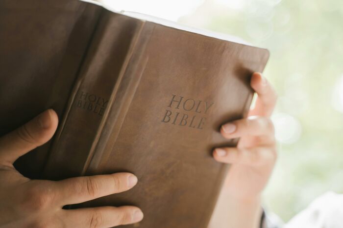 Person holding an old Holy Bible close to face, symbolizing sweet facade hiding manipulation or betrayal in real life.
