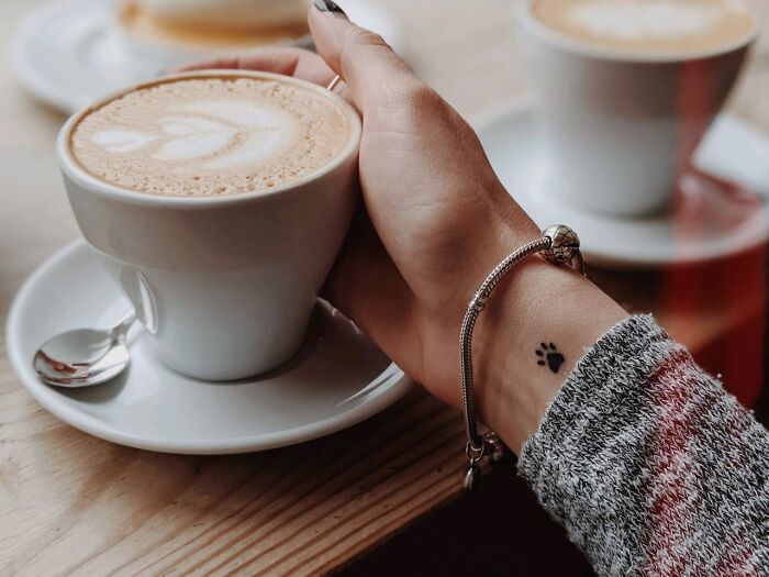 Hand holding a coffee cup showing a small paw print tattoo on the wrist, highlighting unusual client tattoo requests.