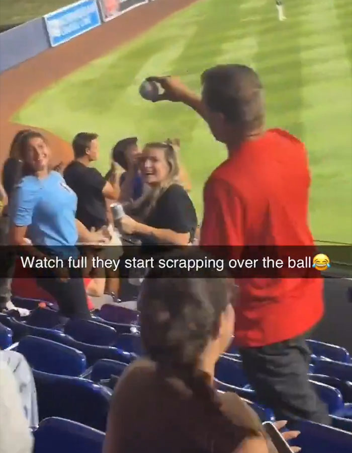Woman in red Phillies shirt holding home run ball at stadium, causing crowd reaction during baseball game incident. Woman in red Phillies shirt holding home run ball at stadium, causing crowd reaction during baseball game incident.