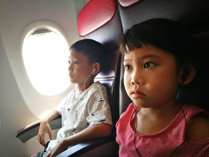 Two children wearing earphones seated on airplane seats, with a window visible beside them during the flight. Two children wearing earphones seated on airplane seats, with a window visible beside them during the flight.