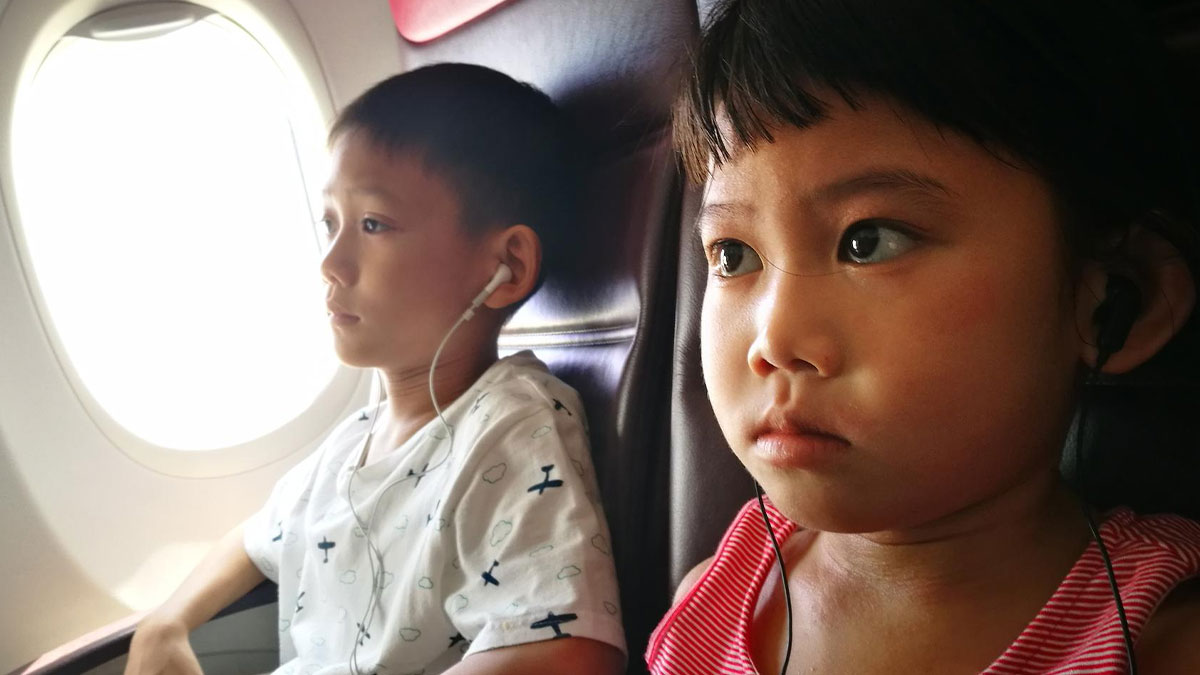 Two children wearing earphones seated on an airplane, showing tense expressions during a dramatic journey conflict.