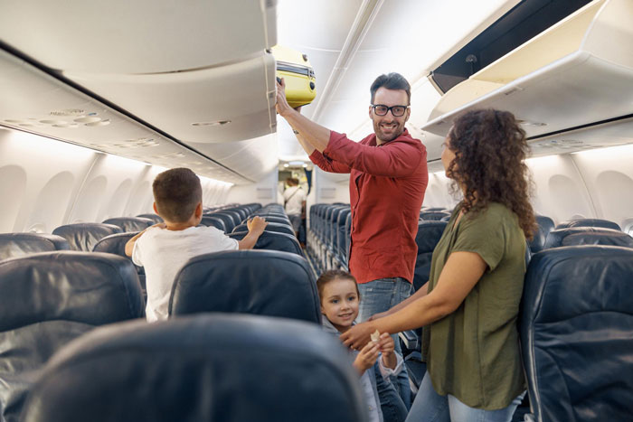 Family watches passenger placing luggage in overhead bin on airplane, creating tension during the journey. Family watches passenger placing luggage in overhead bin on airplane, creating tension during the journey.