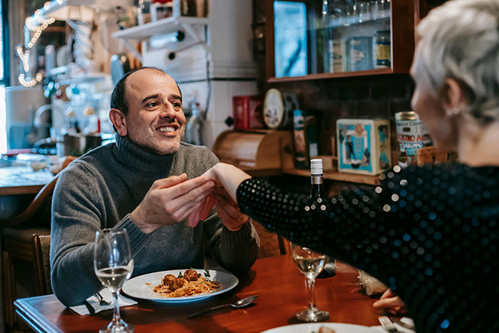 Man in a cozy restaurant holding a woman’s hand, illustrating themes of polyamory and open marriage. Man in a cozy restaurant holding a woman’s hand, illustrating themes of polyamory and open marriage.