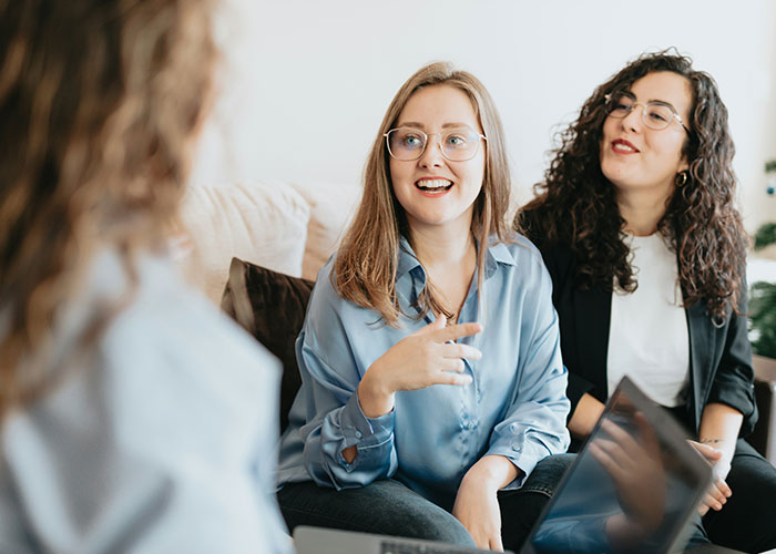 Three women in a meeting, discussing ideas with laptops, illustrating hilarious job descriptions that are technically true.