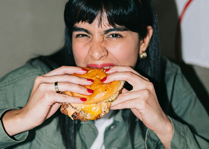 Person manipulating a product by taking a big bite of a cheeseburger, showcasing an expressive reaction.