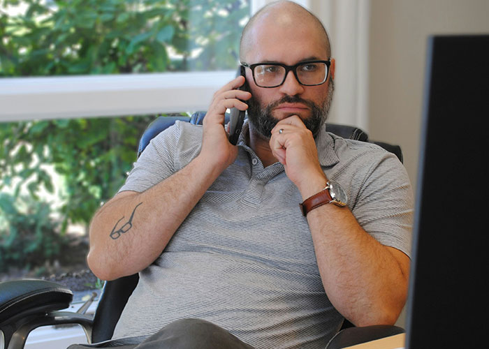 Man with glasses talking on phone in office, showing thoughtful expression related to hilarious job descriptions.
