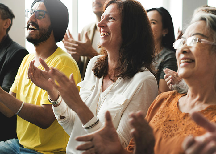 Group of diverse people smiling and clapping, enjoying a moment while discussing hilarious job descriptions about product use.