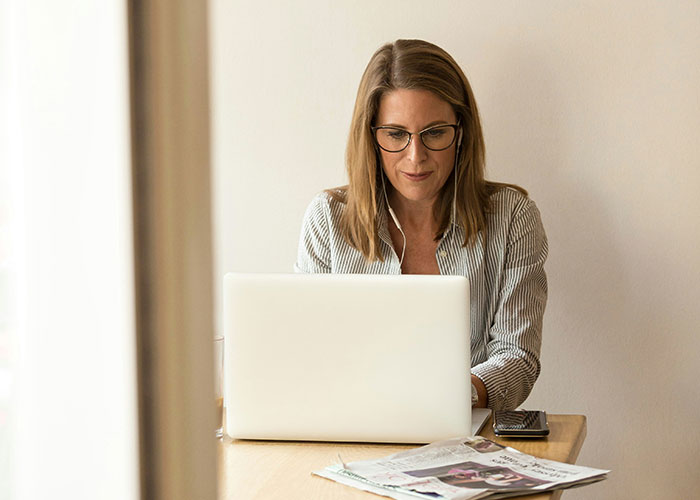 Woman wearing glasses working on a laptop, focused on manipulating person and product in a professional setting.