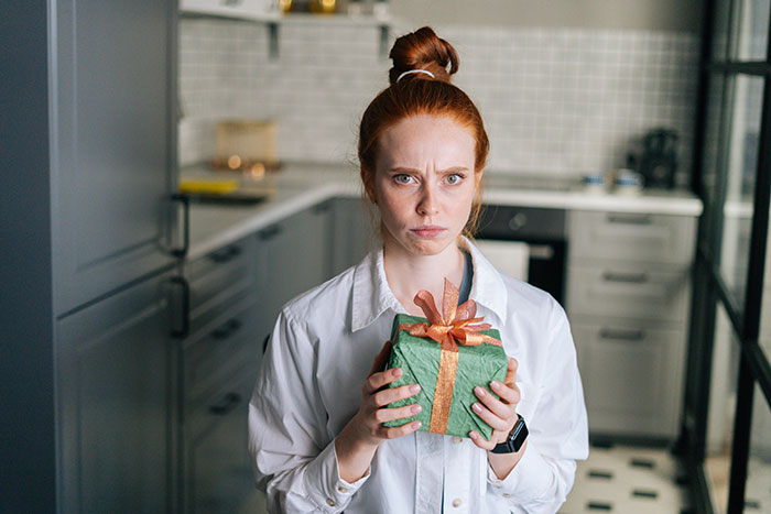 Woman looking horrified holding a wrapped anniversary gift from a guy who considers her his girlfriend after one date Woman looking horrified holding a wrapped anniversary gift from a guy who considers her his girlfriend after one date