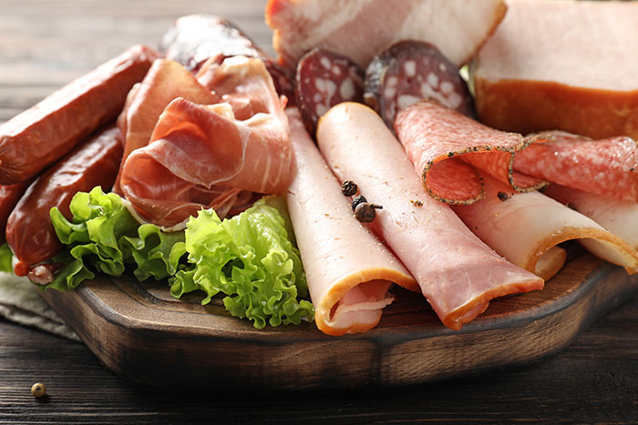 Assorted processed meats on a wooden board with lettuce, highlighting processed meat dementia risk from scientific studies. Assorted processed meats on a wooden board with lettuce, highlighting processed meat dementia risk from scientific studies.