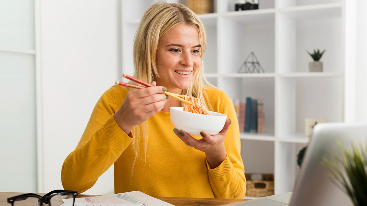 Young woman with a peanut allergy eating noodles at home, reflecting on a serial food thief incident with her roommate.