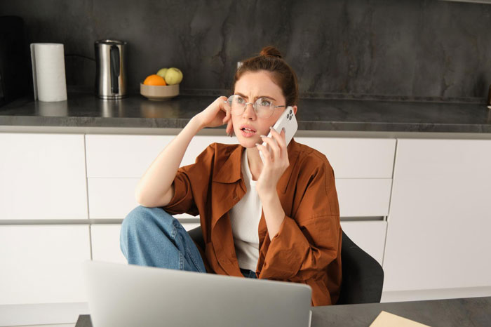 Young woman with glasses in kitchen looking worried while talking on phone, dealing with food allergy and roomie conflict. Young woman with glasses in kitchen looking worried while talking on phone, dealing with food allergy and roomie conflict.
