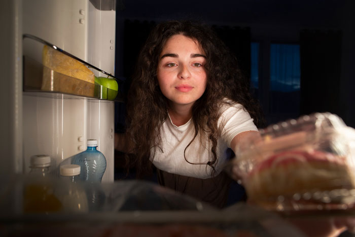 Young woman reaching into fridge at night, illustrating a serial food thief with peanut allergy stealing roommate’s dinner. Young woman reaching into fridge at night, illustrating a serial food thief with peanut allergy stealing roommate’s dinner.