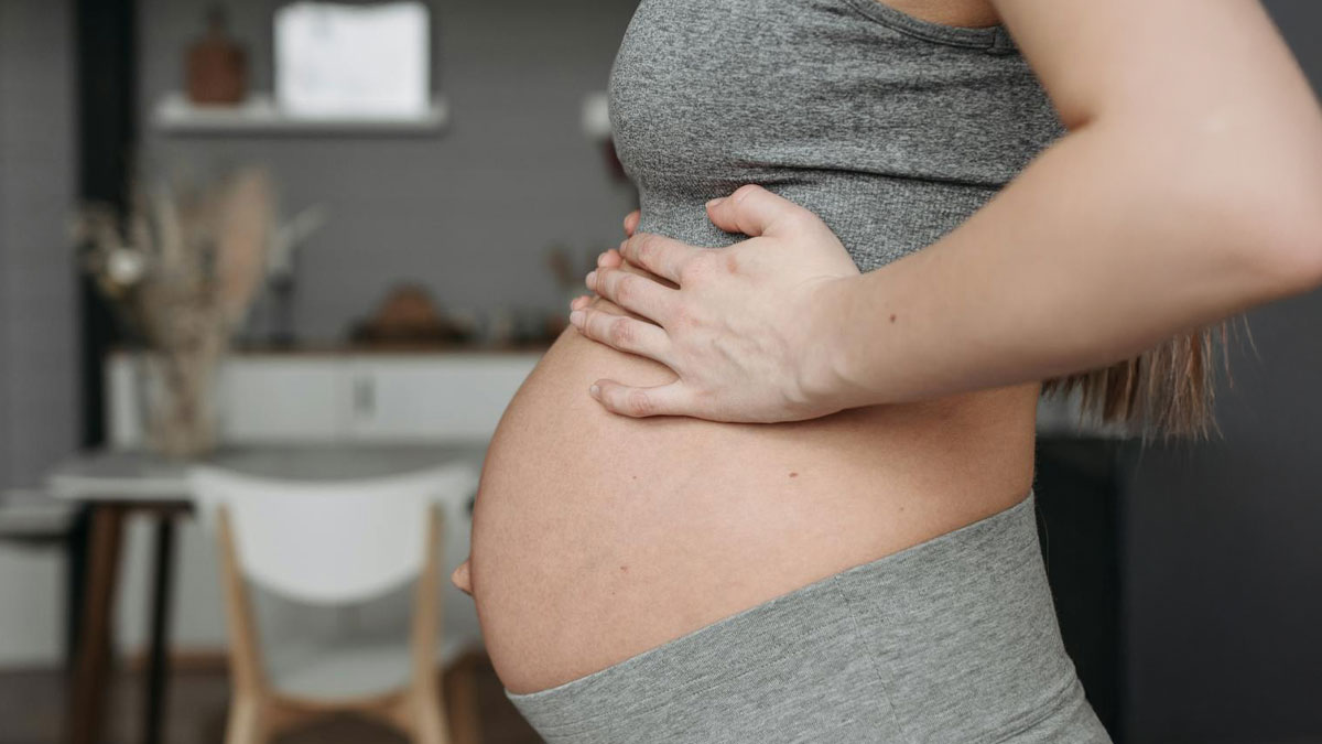 Pregnant woman holding her stomach indoors, illustrating a patient with a rare disease experiencing discomfort.