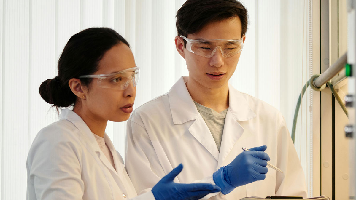 Two doctors wearing lab coats and protective glasses discussing accurate medical diagnoses in a clinical setting.