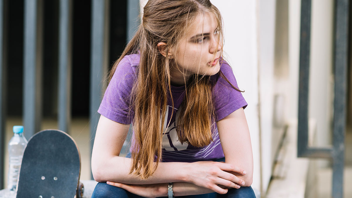 Young woman in a purple shirt sitting by skateboard looking worried, capturing the feeling of scary real-life stories.