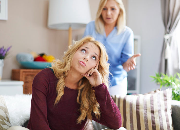Teen girl rolling eyes while mom talks in living room, illustrating hygiene checklist conflict before school drives. Teen girl rolling eyes while mom talks in living room, illustrating hygiene checklist conflict before school drives.