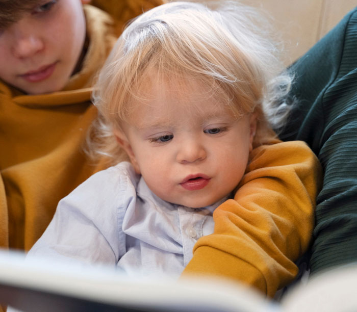 Older sibling reading to a toddler stepsibling, illustrating family moments related to refusing babysit stepsiblings. Older sibling reading to a toddler stepsibling, illustrating family moments related to refusing babysit stepsiblings.