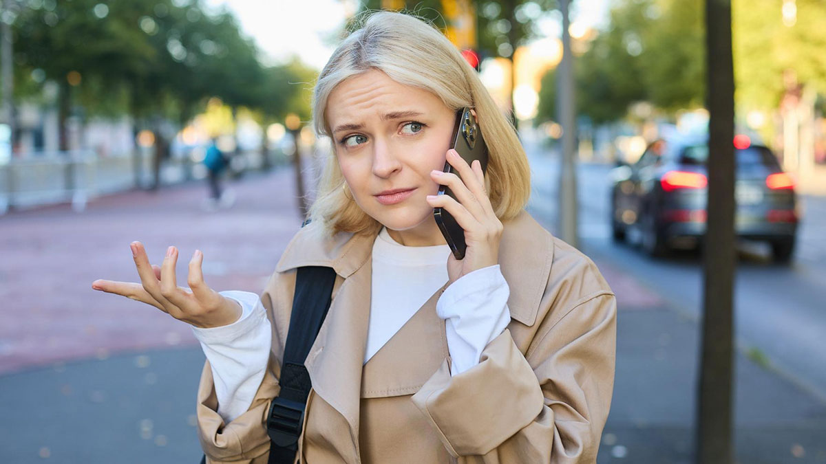 Young woman talking on phone outdoors, showing confused expression while refusing to look after brotheru2019s children.