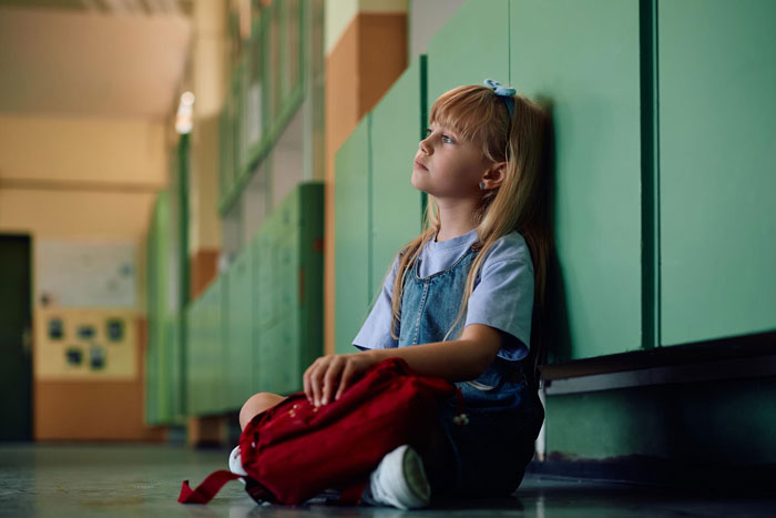 Young girl sitting alone in a school hallway, looking thoughtful, related to cheating guy expecting ex to pick up affair kid. Young girl sitting alone in a school hallway, looking thoughtful, related to cheating guy expecting ex to pick up affair kid.