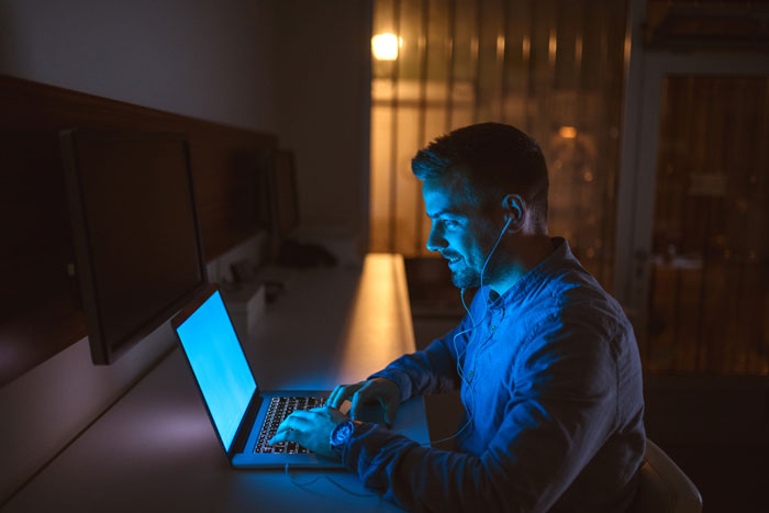 Man in blue shirt uses laptop at night, reflecting on online affair and guilt after ruining marriage. Man in blue shirt uses laptop at night, reflecting on online affair and guilt after ruining marriage.