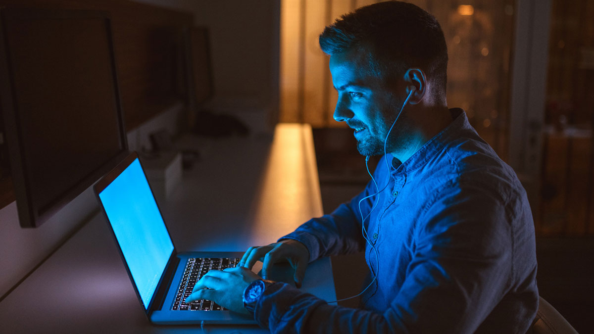Man using laptop late at night, involved in an online affair, reflecting on how he ruined his marriage and feels guilty.