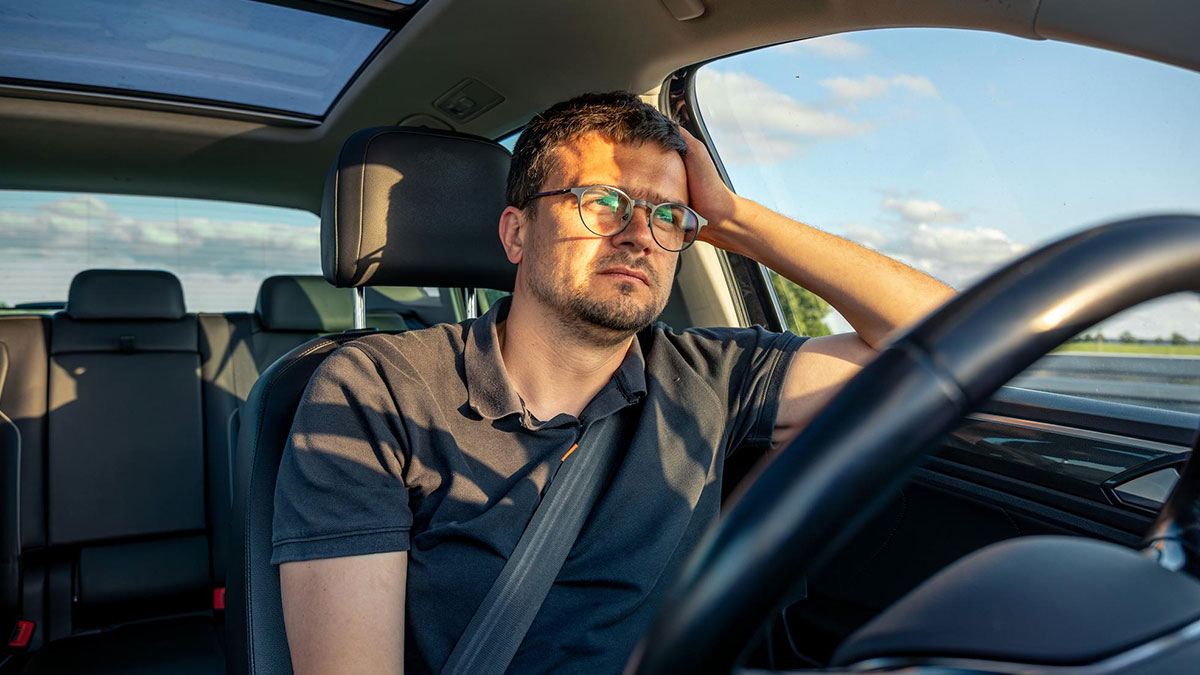 Young man wearing glasses looking frustrated inside a car, related to curfew violation and reporting drunk driver incident