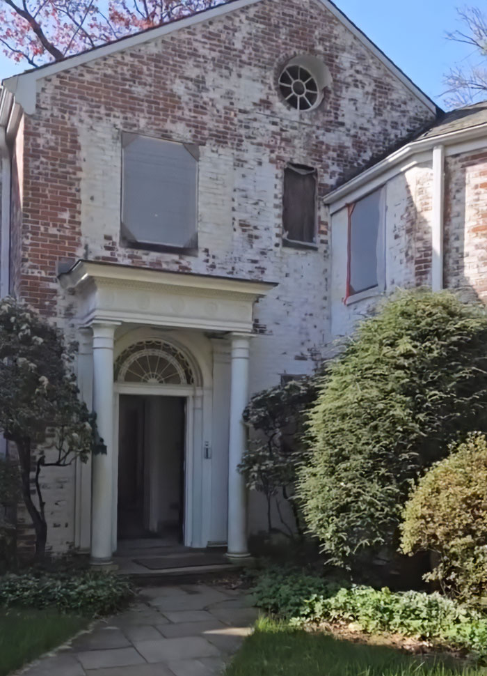 Old brick multimillion-dollar home with boarded windows and classic pillars surrounded by greenery before demolition. Old brick multimillion-dollar home with boarded windows and classic pillars surrounded by greenery before demolition.