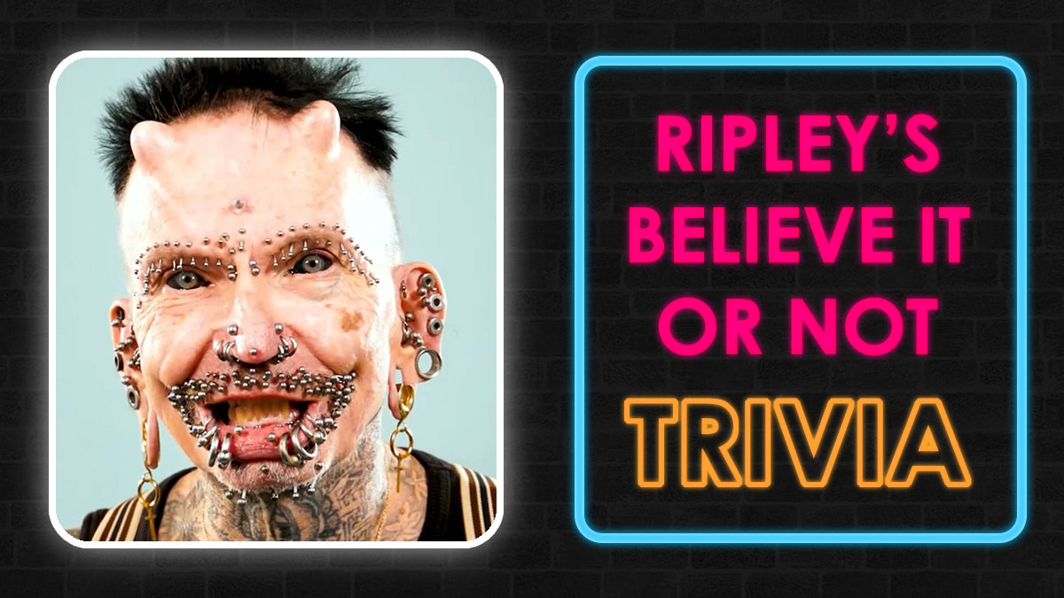Man with extreme facial piercings and tattoos beside neon sign reading Ripley's Believe It or Not trivia quiz