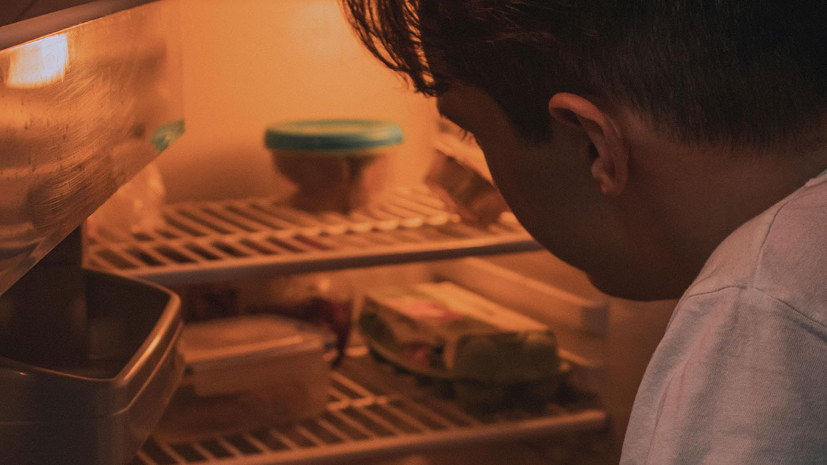 Person looking inside fridge with leftovers, hinting at a habanero cake prank to stop roommate stealing food.