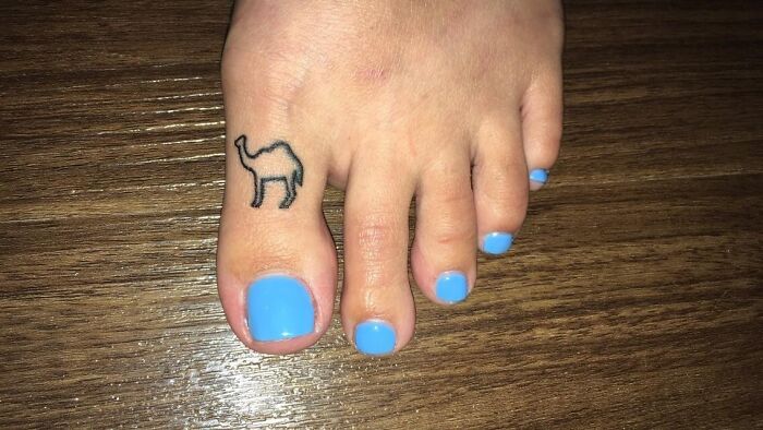 Close-up of a foot with blue nail polish and a small camel tattoo on the toe, illustrating unusual client tattoo requests.
