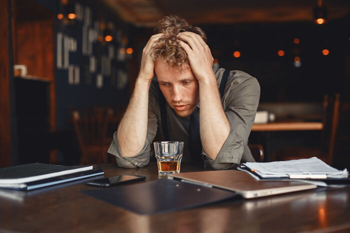 Young man looking stressed at a table with a drink and papers, illustrating hilarious ways to ruin a first date.