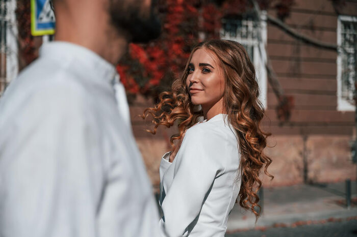 A stylish woman with curly hair smiling during a first date outdoors, capturing hilarious ways to ruin a first date.