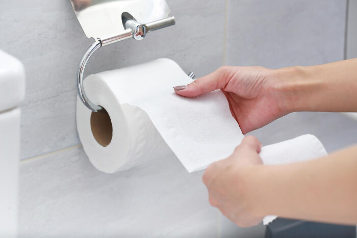 Person pulling toilet paper from a roll in a bathroom, illustrating a funny way to ruin a first date scenario.