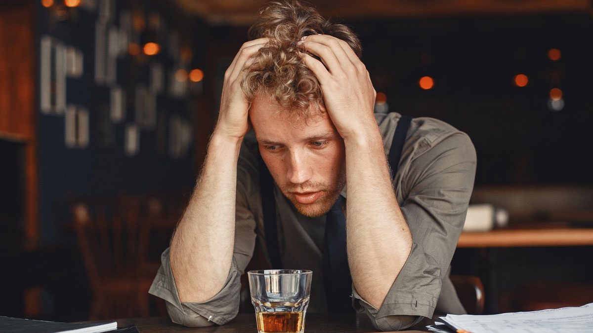 Man sitting at table looking stressed with drink nearby, illustrating ways to ruin a first date in 60 seconds.
